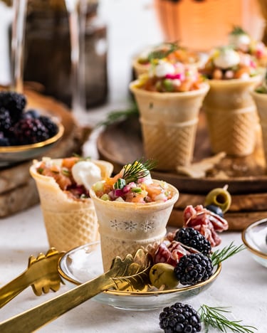Mehrere Waffeln mit Räucherlachs-Tatar stehen dekoriert zwischen Brombeeren auf einem Tisch.
