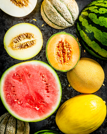 Buntes Allerlei verschiedener Melonenarten, teils ganz, teils halbiert, als Topshot vor dunkelgrauem Hintergrund