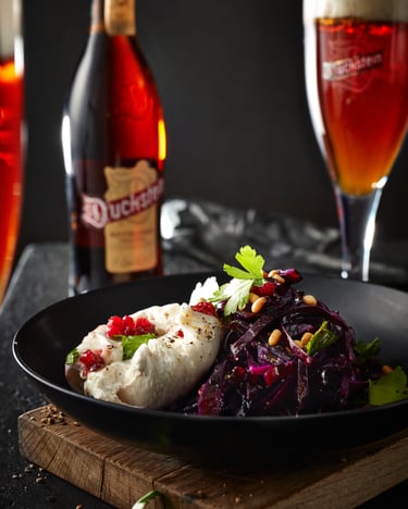 Ein schwarzer Teller mit Burrata auf Rotkohl mit Preiselbeersauce neben einer Flasche und einem Glas mit Duckstein