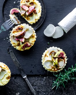 Mini-Quiche mit Ziegenkäse und frischen Feigen auf Schieferplatte mit Rosmarin und Ziegenkäserollen.