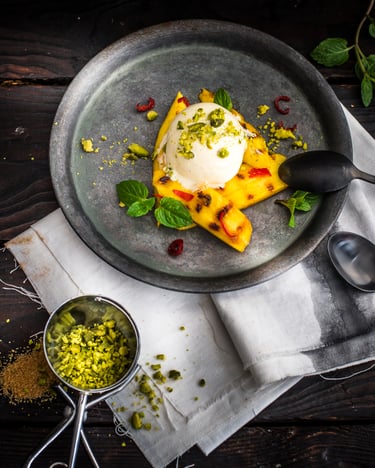 Gegrillte Mango mit Chili auf dunklem Untergrund, daneben gehackte Pistazien als Deko