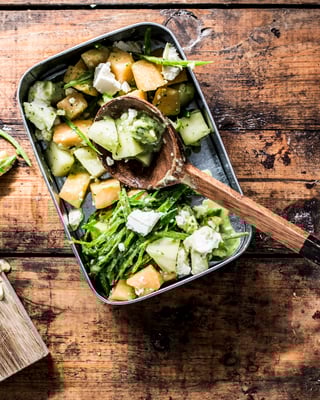 Auf einem Holzuntergrund steht ein Behältnis. Darin Melonensalat