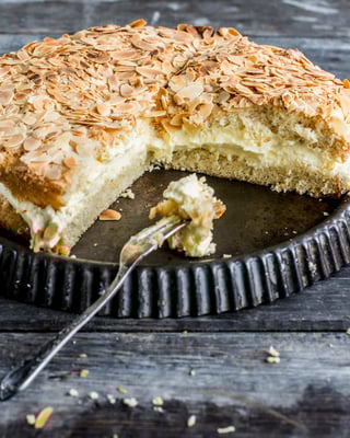 Angeschnittene Bienenstichtorte mit Mandeln auf einer umgedrehten Tarteform mit einer Kuchengabel