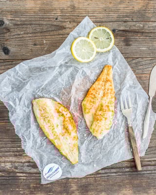 Auf Holzuntergrund liegen zwei gebratene Fischfilets