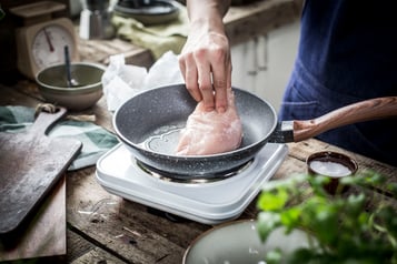 Ein Stück Hähnchenbrust wird in eine Pfanne mit Öl gelegt