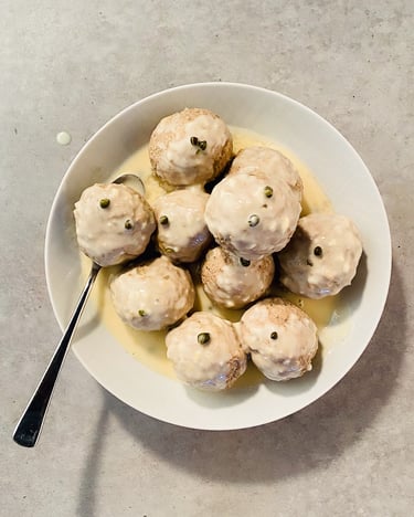 Ein Berg aus Königsberger Klopsen auf einem weißen Teller mit Sauce.