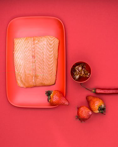 Lachs auf rotem Teller und rotem Untergrund mit Chili und Erdbeeren