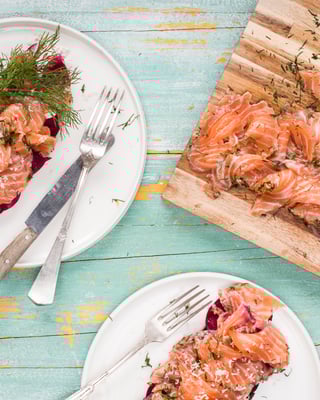 Auf einem Teller liegt angerichteter Graved Lachs, daneben ein Brett mit Lachs und Dill