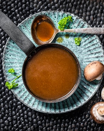 Selbstgemachte Bratensauce mit Pilzen in einer Schale mit Schöpfkelle