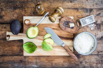 Auf Holzuntergrund liegen eine aufgeschnittene Avocado und weitere Zutaten
