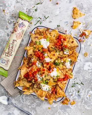 Voll geladene Schale mit gratinierten Flammkuchen-Nachos und einem Topping aus Schmand, Frühlingszwiebeln, Bacon, Chili und Tomaten
