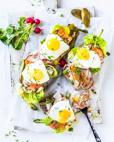 Zwei Brote sind so dick mit Salat, Radieschen, Krustenschinken und Spiegelei belegt, dass man das Brot kaum sehen kann.