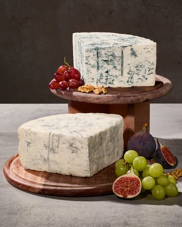 Zwei Gorgonzola-Viertel auf Holzbrettchen angerichtet mit Obst und Nüssen.
