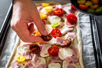 Halbierte Kirschtomaten werden auf der Blech-Quiche verteilt