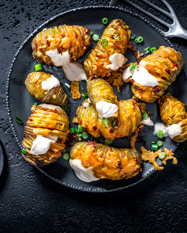 Mehrere Hasselback-Kartoffeln liegen auf einem schwarzen Teller