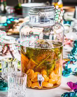 Fruchtige Bier Bowle mit Mandarinen, Sekt und Pfirsichlikör und Zitronenmelisse im Glas auf einem bunt geschmückten Partytisch
