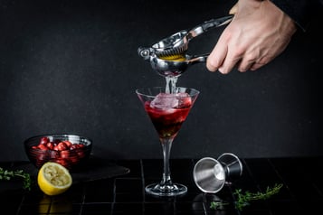 Eine Zitrone wird in ein Glas mit roter Flüssigkeit ausgepresst