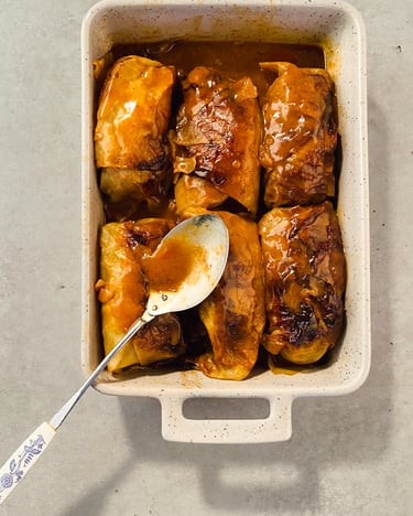 Mehrere Kohlrouladen in einer Auflaufform. Darauf liegt ein Löffel mit Sauce.