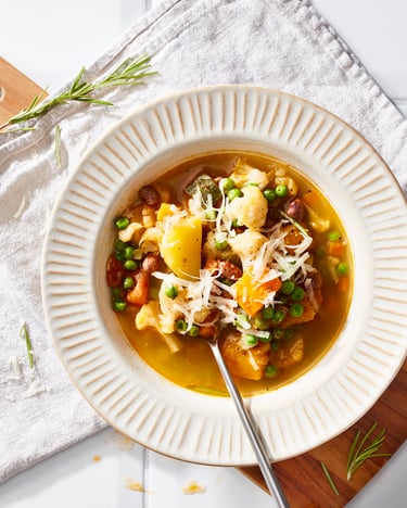 Weißer Teller mit Randmuster mit Minestrone (Gemüsesuppe) darin auf hellem Untergrund