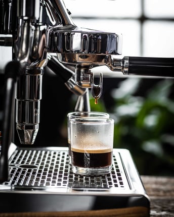 Glänzende Siebträgermaschine, durch die gerade der letzte Tropfen Kaffee ins Glas fällt