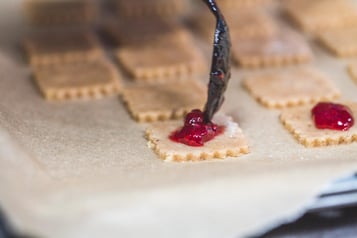 Marmelade wird mit einem Löffel auf die Plätzchen gegeben.
