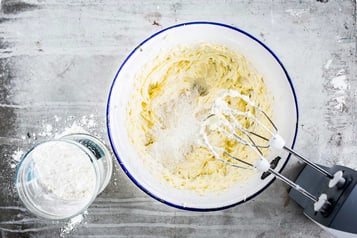 In einer weißen Schüssel befindet sich Teig, daneben ein Handrührgerät mit Schneebesen