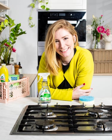Jules in einer aufgeräumten hellen Küche mit frischen Blumen und Reinigungsprodukten in einem Korb