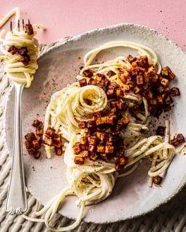 Auf einem pinken Tisch steht ein Teller mit einer Portion veganer Carbonara