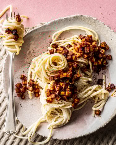 Auf einem pinken Tisch steht ein Teller mit einer Portion veganer Carbonara