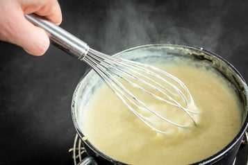 Die Creme befindet sich in einem Topf, eine Hand mit einem Schneebesen rührt darin