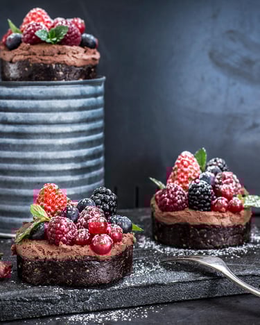 Kleine Schokoküchlein mit Beeren und Puderzucker auf einer Konserve ohne Label und einer Steinplatte vor dunklem Hintergrund.