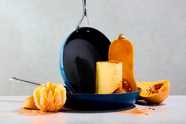 Zwei Pfannen angerichtet, umgeben von orangenem Gemüse und Obst