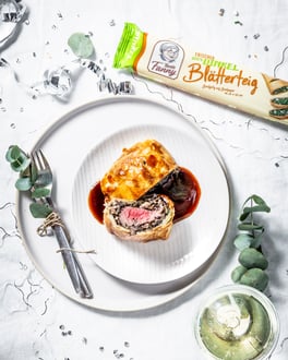Mini-Filet Wellington auf weißem Teller und festlich geschmücktem Tisch