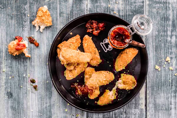 Frittierte Mozzarella Sticks liegen auf einem schwarzen Teller, daneben auch ein Glas mit Dip.