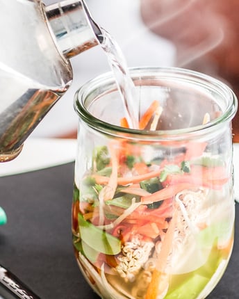 Zutaten für eine selbst gemachte Pho Instantsuppe in einem Einmachglas steht auf einem Schreibtisch und wird als schnelles Büro-Essen mit heißem Wasser aus einem Wasserkocher übergossen
