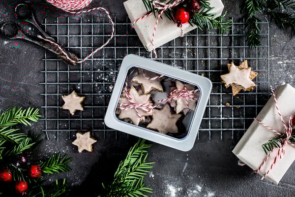 Plätzchen in einer Keksdose mit weihnachtlichem Schmuck sowie einer Schere und rot-weißer Schnur