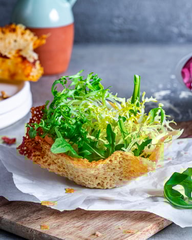 Grüner Salat im Parmesankörbchen auf Holzbrett mit Parmesankörbchen und Parmesanverpackung im Hintergrund