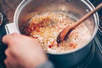 Chili wird in einem großen silbernen Topf in Öl angeschwitzt und mit einem Holz-Kochlöffel verrührt.