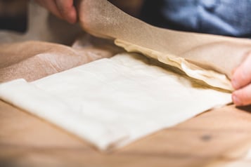 Ein Pizzateig auf einem Backpapier wird an den Seiten eingeklappt