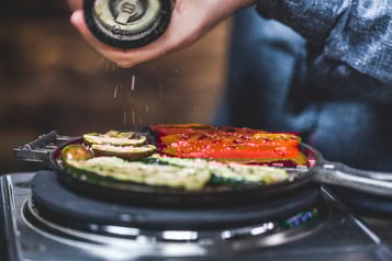 Champignonscheiben, Paprika und Zucchini in einem Waffeleisen werden mit einer Pfeffermühle gewürzt.