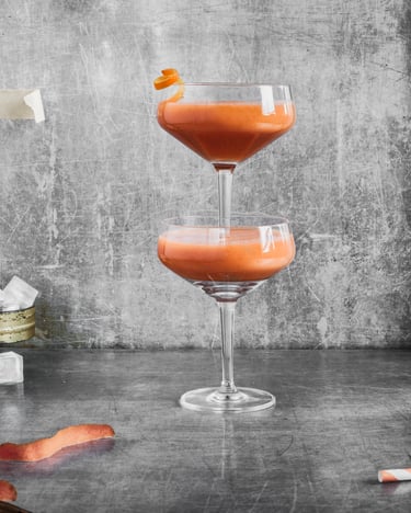 Zwei gestapelte Martinigläser mit orangenem Smoothie gefüllt vor grauem Grund