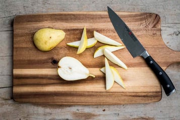 Auf einem Holzbrett liegen Birnenspalten, daneben ein Messer