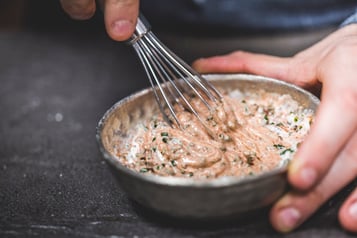 Ein beiger Dip mit Kräutern wird mit einem kleinen Schneebesen gerührt.