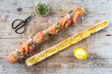 Auf Holzuntergrund liegen Zutaten für ein Lachs-Baguette