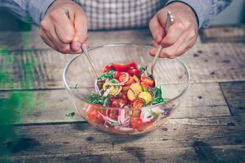 Ein Tomatensalat mit Zwiebeln in einer großen Glasschüssel wird mit zwei Esslöffeln vermengt