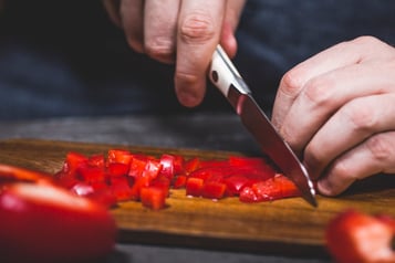 Auf einem Holzbrett wird Paprika in Würfel geschnitten