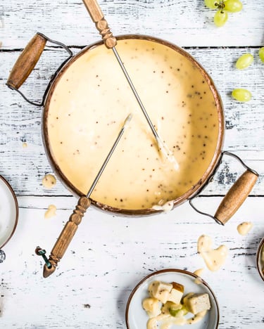 In der Mitte eines Tisches steht ein Topf mit Käsefondue. Daneben Schalen mit Brot