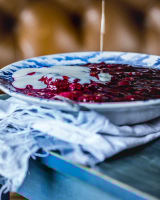 In eine Schüssel mit roter Grütze wird Vanillesauce getropft
