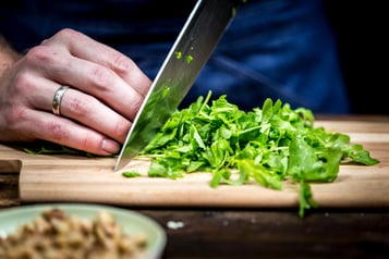 Rucola wird auf einem Holzbrett mit einem großen Küchenmesser geschnitten