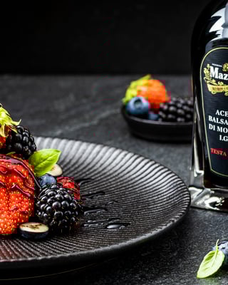 Verschiedene Beeren mit Balsamico-Topping, dahinter steht eine Flasche Balsamico